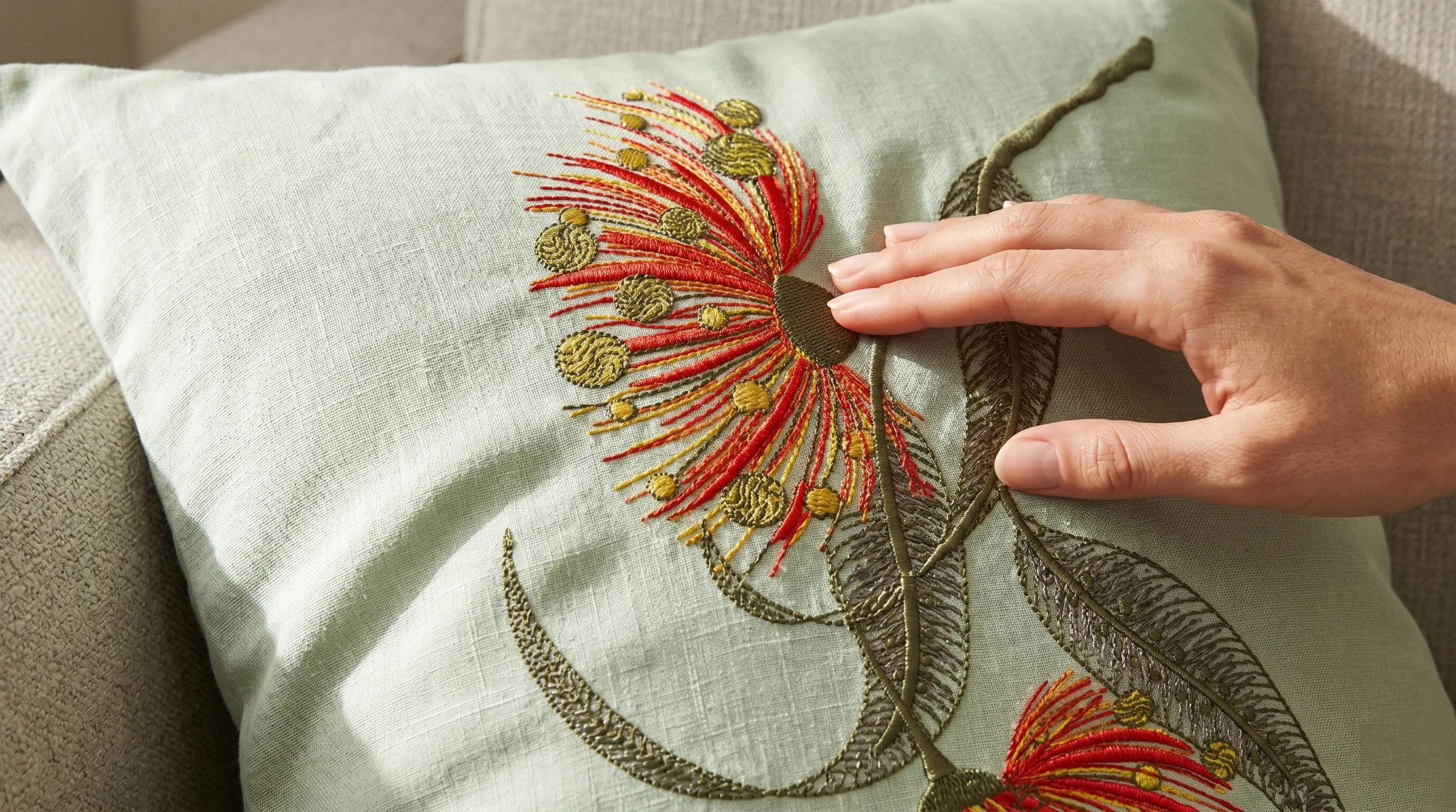 Hand touching embroidered eucalyptus cushion on linen sofa